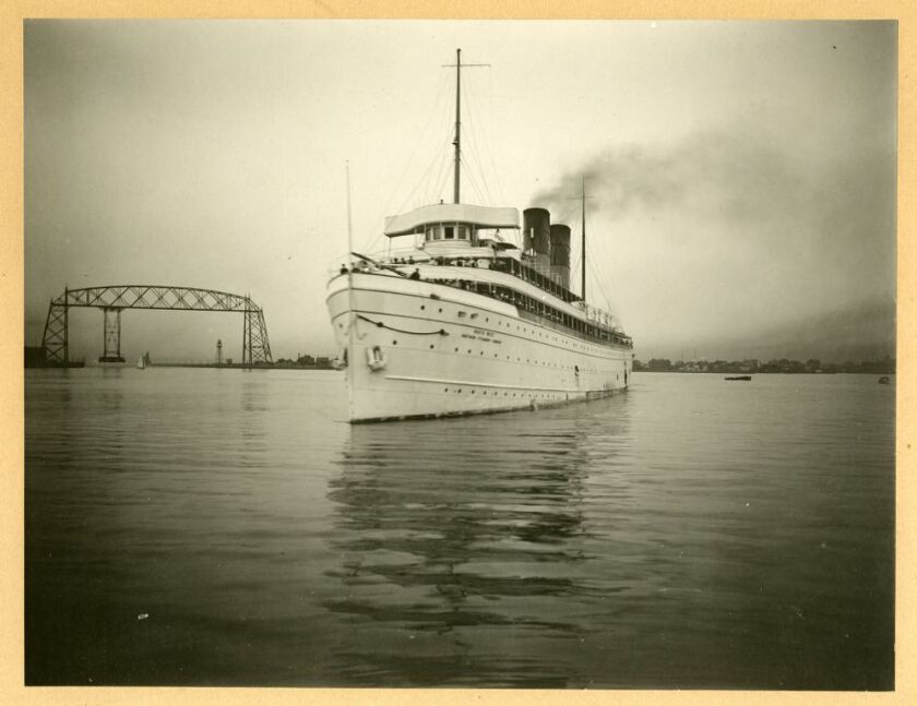 A black and white photo of  a ship in front of a bridge